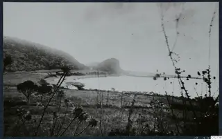 Landscape at Vouni with a scrub-covered hillside, a rocky knoll and a pale stretch of water in the middle distance