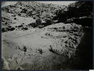 Excavated stone foundations of the Paradisiotissa temple at Vouni, seen from the north-west, with a rocky hillside behind.