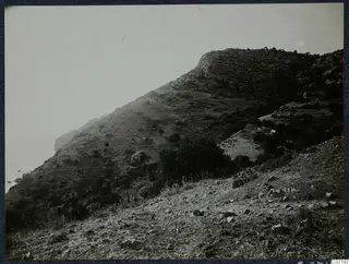 Steep scrubby hillside falling to the sea at Vouni, with rocky ground in the foreground.