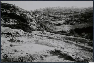 Rocky, scrub-covered hillside above an excavated area with exposed stone foundations at Vouni