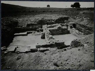 Excavated stone walls and a paved floor at Soli, Cholades, with trees on the hill behind.