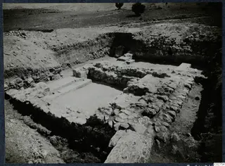 Excavated stone walls and a paved floor with steps at Soli, with trees and hills in the background.