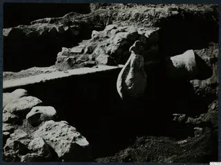Carved stone figure standing in an excavated trench among wall remains at Cholades, Soli.