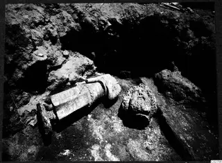 Carved stone statue lying on its side and a carved head in situ in an excavated room at Soli
