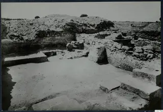 Excavated area at Soli with stone walls, large flat slabs and earth banks rising behind