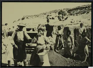 Men and women working in an excavation cutting at Mersinaki, one woman with a bucket and another laughing at the camera.