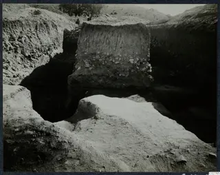 Soil profile in the excavation at Mersinaki, a standing earth face with embedded stones and a tree on the hill behind.