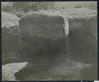 Soil section from the excavation at Mersinaki, with a stone wall and pale earth mound to the left.