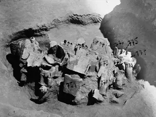 Broken stone statue fragments lying in an excavated pit at Mersinaki, with numbered labels on several pieces