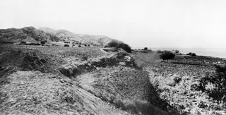 View towards Vouni from the excavation at Mersinaki, with low walls, rocky hills and the sea beyond.