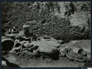Statue fragments lying together in an excavation at Mersinaki, with a carved face and heads visible among broken bodies.