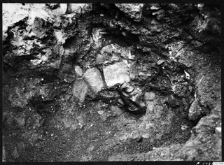 Carved stone head partly embedded in soil among stone blocks, in situ in excavation H 15 at Mersinaki