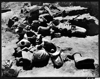 Excavation at Mersinaki showing a heap of broken sculpture fragments, including a head and a foot, lying in the soil.