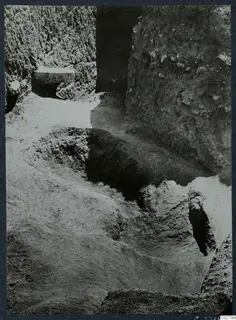Excavated pit at Mersinaki with steep earthen sides and a flat stone slab set into the left-hand wall.
