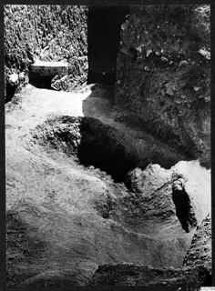 Excavated pit at Mersinaki with steep earth walls and a flat stone slab set into the upper left wall