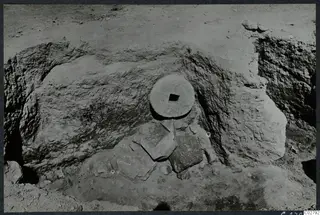 Excavation at Mersinaki with a round stone disc with a square hole set against a cut earth face.