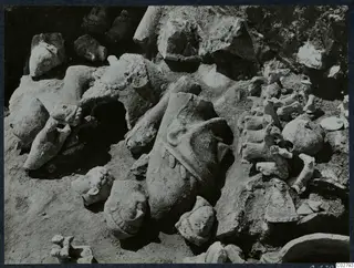 Statue fragments lying in an excavation at Mersinaki, including a large head with a conical hat in the middle