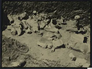 Broken stone sculpture fragments lying in excavated soil at Mersinaki, including several heads, a hand and body pieces