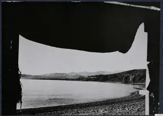 View through a tent opening over a calm bay with a pebble beach and hills at Mersinaki