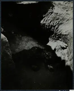 Objects lying in situ in an excavated pit at Mersinaki, with pale soil walls and dark shadow across the floor.