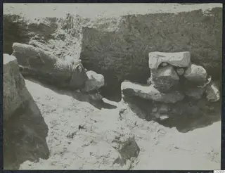 Stone objects lying in situ in a trench at Mersinaki, Pit II, with an earth section behind them