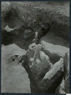 Pale stone objects lying in situ in Pit VI at Mersinaki, with soil banks of the excavation around them.