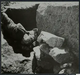 Excavation pit at Mersinaki with large pale stone blocks and a rolled dark bundle among the finds in situ