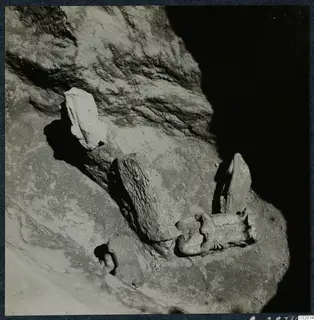 Sculpture fragments lying in situ in excavated ground at Mersinaki, set against a rock face