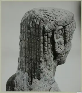 Carved limestone head and upper body of a statue from Kition, seen from the side, with grooved hair.