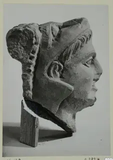 Carved stone head in profile facing right, from Kition, shown on a wooden block