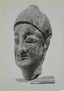 Limestone head with a tall, rounded headdress and almond-shaped eyes, shown in three-quarter view resting on a wooden block