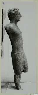 Limestone statue of a standing figure in profile, facing right, with arms and lower legs broken off