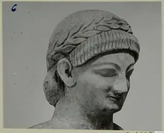 Limestone head and upper shoulders of a statue, with a leaf-carved band over the hair and eyes lowered, from Kition