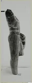 Limestone statue fragment of a standing figure in a draped garment, shown in side view