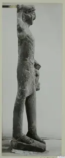 Side view of a standing limestone statue with one arm raised to the top of the head, on a rectangular base