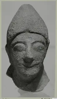 Limestone head statue fragment from Kition with a tall pointed headdress and a slight smile