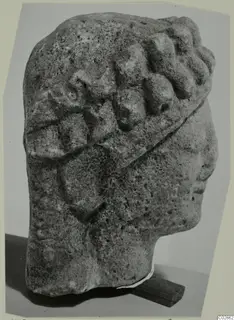 Limestone head fragment from Kition, in profile facing right, with rows of curled hair and a band across the head.