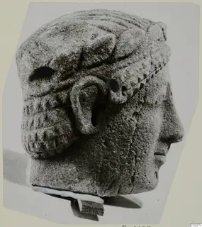 Limestone head in right profile, wearing a wide band with ridged decoration, set on a small stone base.