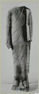 Limestone statue of a standing headless figure in a draped garment with diagonal folds