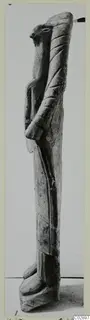 Limestone sculpture fragment of a tall standing figure with a beak-like head, photographed on a mounted card