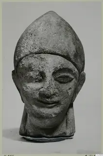 Limestone head of a figure wearing a tall pointed cap, from Kition, photographed against a plain grey background