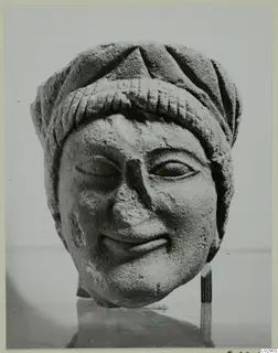 Carved limestone head with a wrapped headdress and slight smile, seen from the front