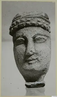 Limestone head of a figurine with a banded headdress and carved face, photographed against a plain grey background