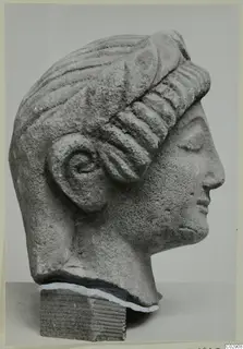 Limestone head from Kition, shown in profile facing right, with ridged wavy hair and a carved ear.