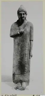 Limestone statue of a standing figure from Kition, with a tall cap and arms folded across the chest.