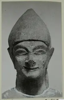Limestone head of a statue from Kition, wearing a tall pointed cap, with a broad smile and narrowed eyes