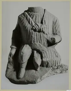 Limestone seated figure, headless, with draped garment and bent arm, shown against a plain grey background