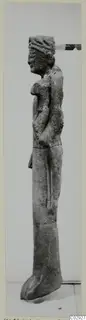 Limestone statue of a standing figure, seen in side view, with arms folded across the chest.