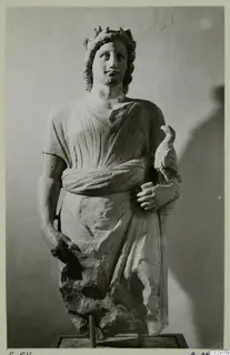 Carved stone statue of a standing figure with a leafy wreath, holding a small bird against its side, on a square base.