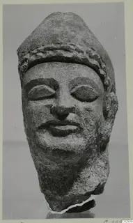 Limestone head with a band-decorated headdress and downcast eyes, from Kition, photographed frontally against a grey background.